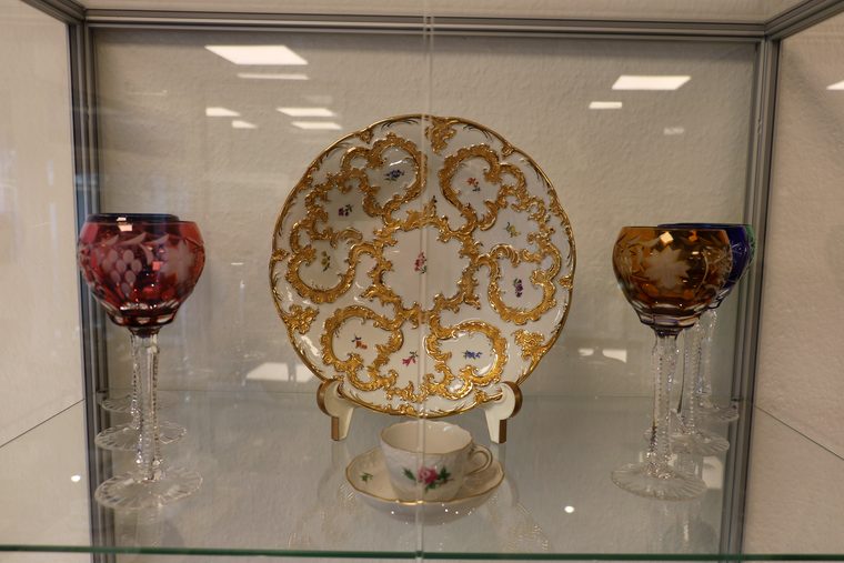 Reich vergoldeter antiker Zierteller zwischen zwei böhmischen Kristallgläsern in der Vitrine