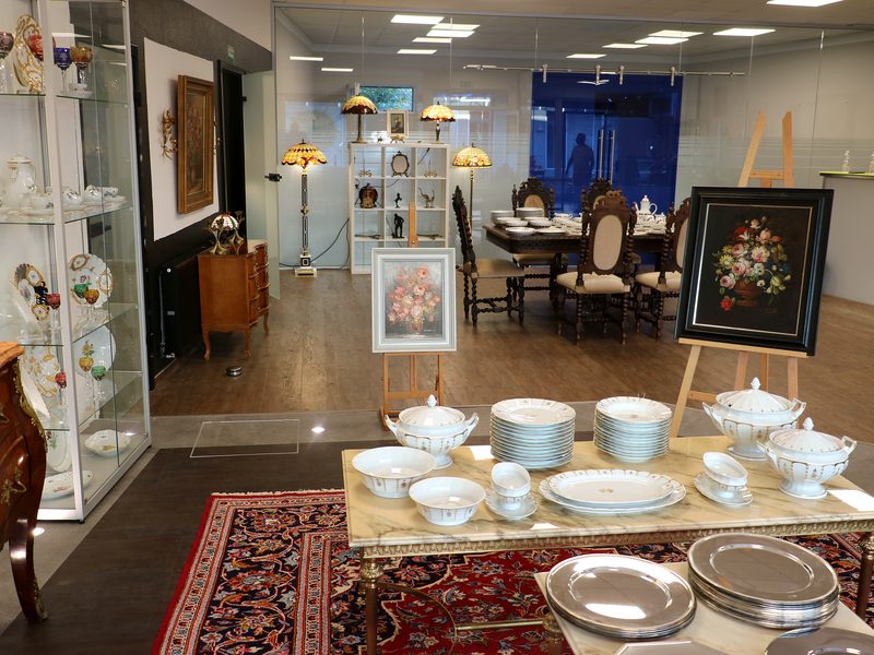 Blick in den Showroom mit antikem Esstisch, gedecktem Porzellan, Gemälden und Vitrinen – Verkauf im Auftrag