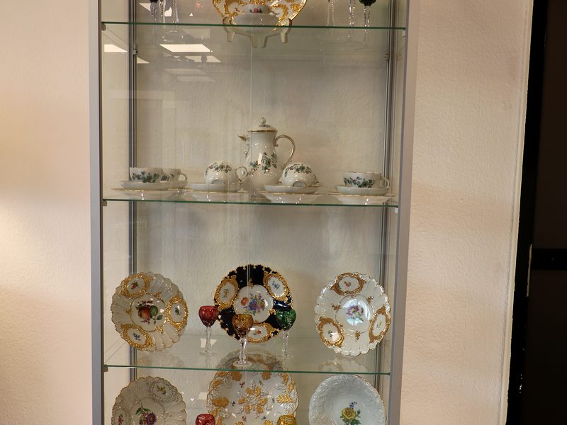 Sammlung antiker Porzellanteller und böhmischer Kristallgläser in einer beleuchteten Glasvitrine