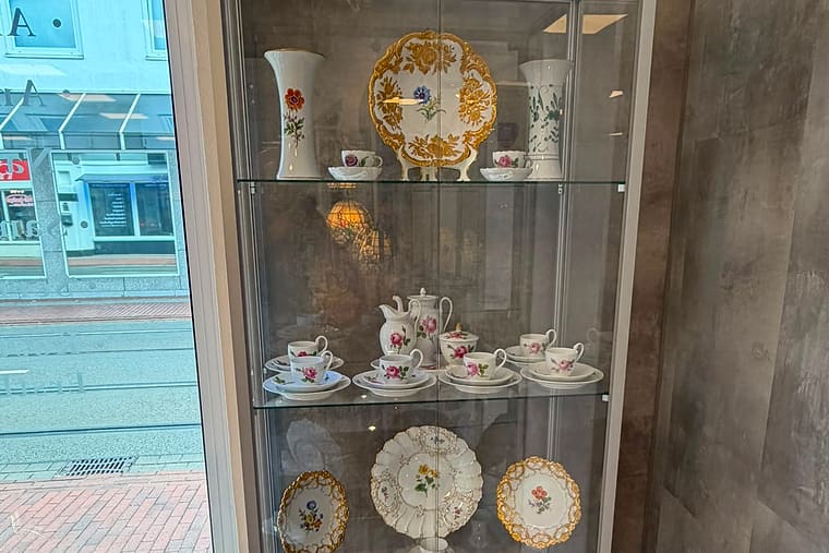 Vitrine am Schaufenster mit antikem Blumen-Porzellan, Kaffeeservice und vergoldeten Ziertellern